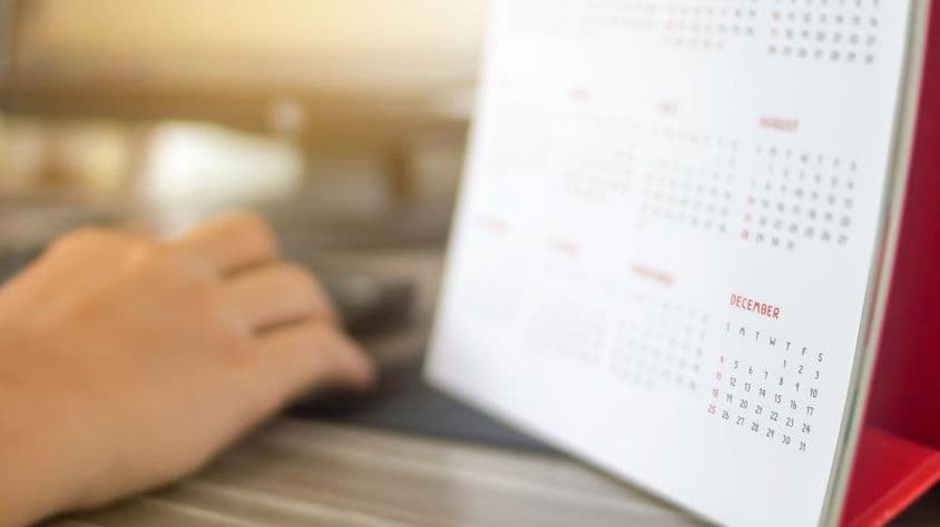 एक हाथ कैलेंडर के बगल में, महीनों के साथ धुंधला, दिसंबर स्पष्ट रूप से दृश्य।