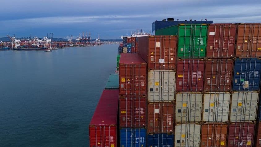 बाईं ओर एक समुद्री बंदरगाह की खाड़ी दिखाई दे रही है, दाईं ओर ढेर किए गए कंटेनर।