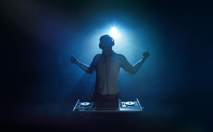 एक व्यक्ति डीजे बूथ के पीछे खड़ा है।