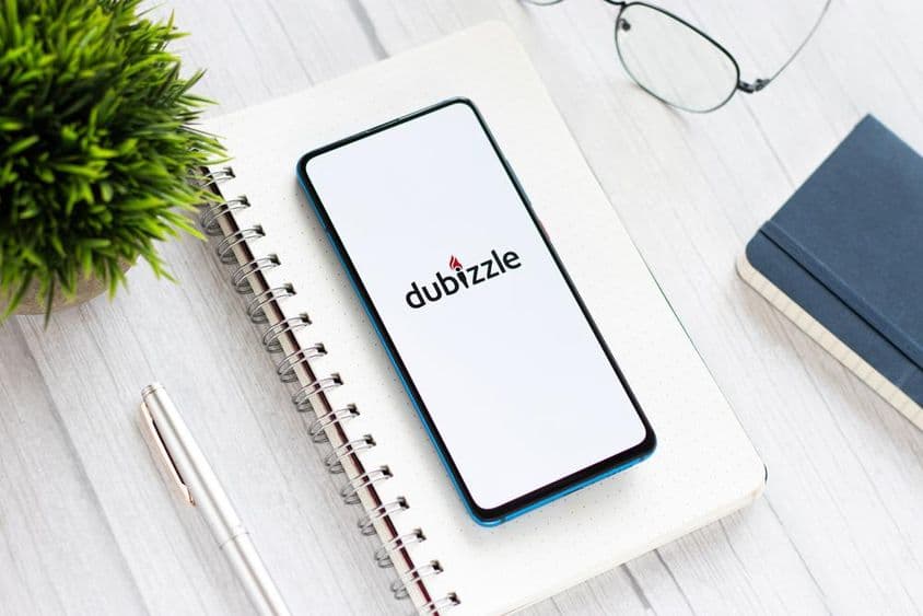 टेबल पर नोटपैड के नीचे, चश्मे और हरे पौधे के साथ, डुबिजल चलाते हुए एक फोन।