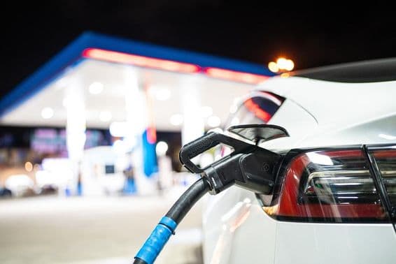 टेस्ला को चार्ज किया जा रहा है, पृष्ठभूमि में एक गैस स्टेशन।