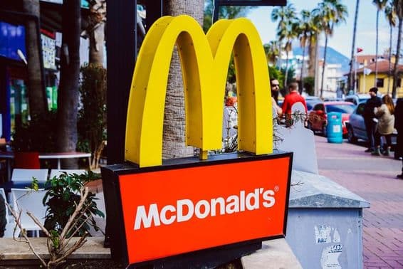 मैकडॉनल्ड्स का साइन, पृष्ठभूमि में सड़क दृश्य के साथ।