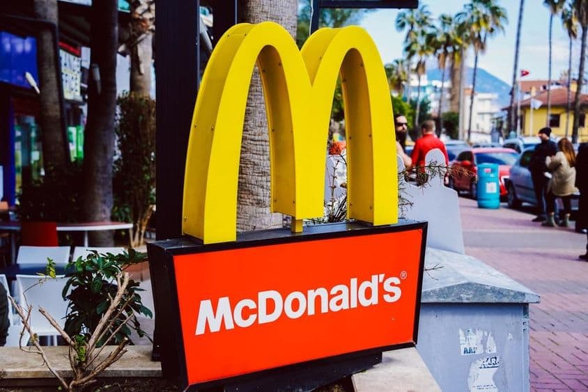 मैकडॉनल्ड्स का साइन, पृष्ठभूमि में सड़क दृश्य के साथ।