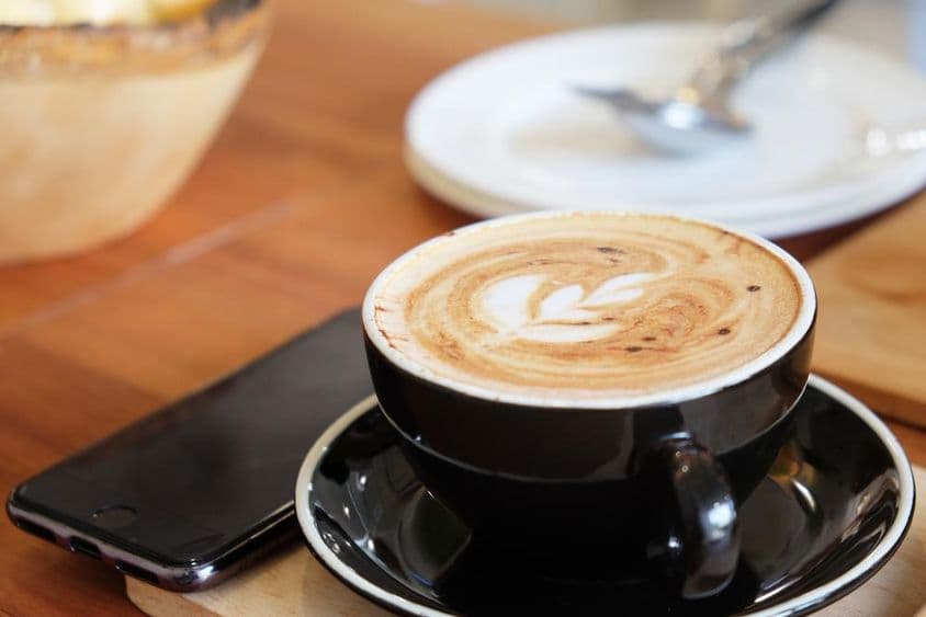 टेबल पर रखा कपुचिनो और उसके बगल में रखा हुआ फोन।