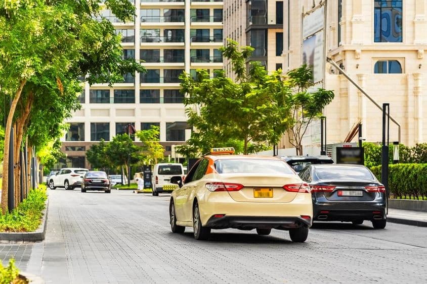 दुबई की सड़क पर कारें, अग्रभूमि में टैक्सी, पीछे घर।