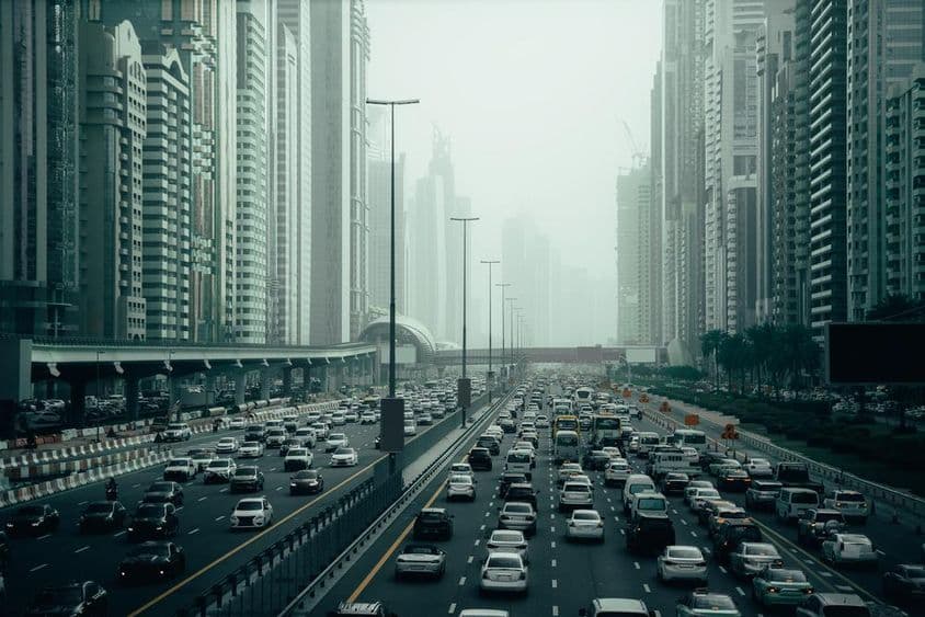 दुबई के शहर में भीड़भाड़ वाला हाईवे, 2x7 लेन, दोनों तरफ गगनचुंबी इमारतें।