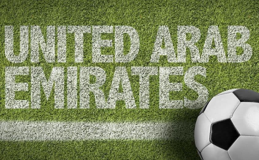 घास पर चित्रित यूएई का शिलालेख और एक फ़ुटबॉल।