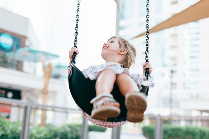 खुशहाल छोटी बच्ची किंडरगार्टन के यार्ड में झूला झूलते हुए।