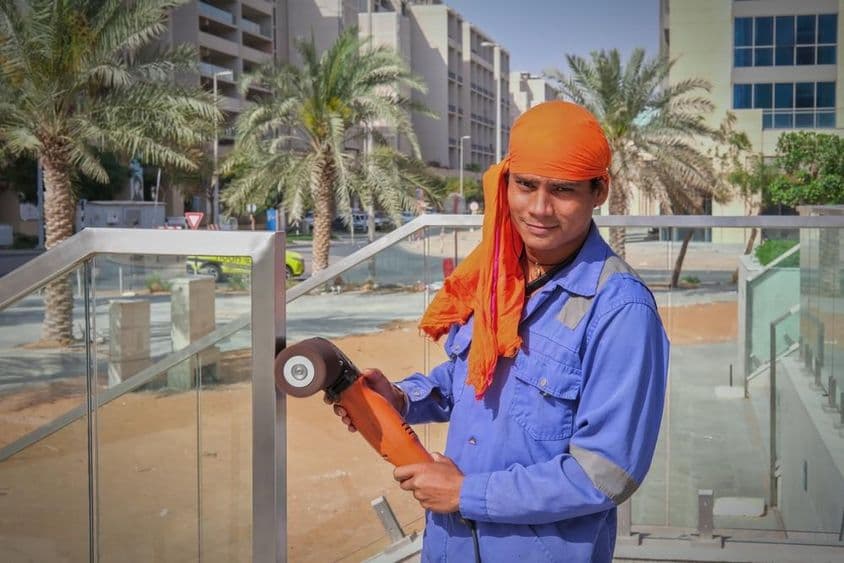 दुबई में रेलिंग की पॉलिश करता श्रमिक।