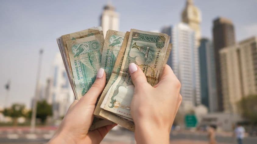 दुबई की गगनचुंबी इमारतों के सामने यूएई मुद्रा पकड़े एक लड़की।