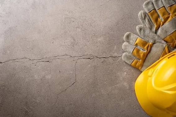 ब्रेक समय, पीला हेलमेट और कार्य दस्ताने एक दरार वाले कंक्रीट सतह पर रखे हुए।