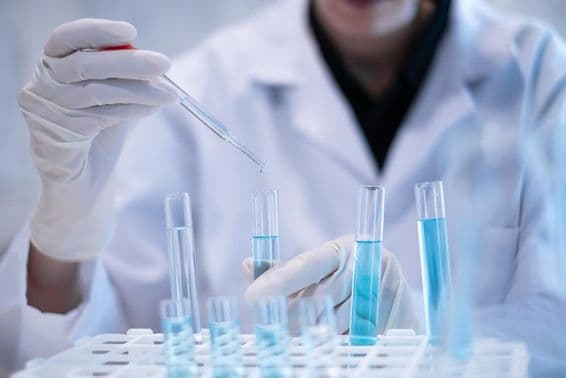 प्रयोगशाला में एक वैज्ञानिक टेस्ट ट्यूब में नीले तरल का पिपेटिंग करते हुए।