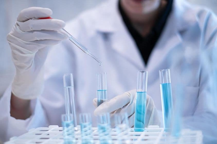 प्रयोगशाला में एक वैज्ञानिक टेस्ट ट्यूब में नीले तरल का पिपेटिंग करते हुए।