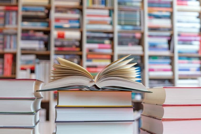 शेल्फ के सामने किताबों के ढेर पर खुली हुई उपन्यास