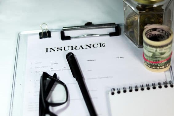 बीमा फॉर्म के साथ सिक्कों की डिब्बी, डॉलर का बंडल, पेन और चश्मा।