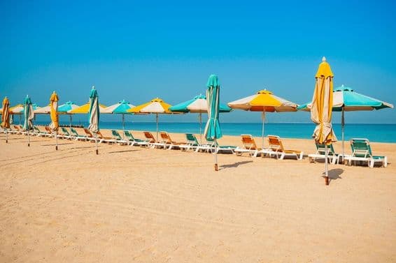 दुबई सार्वजनिक बीच, रेतीला तट, सन लाउंजर्स और नीला समुद्र।