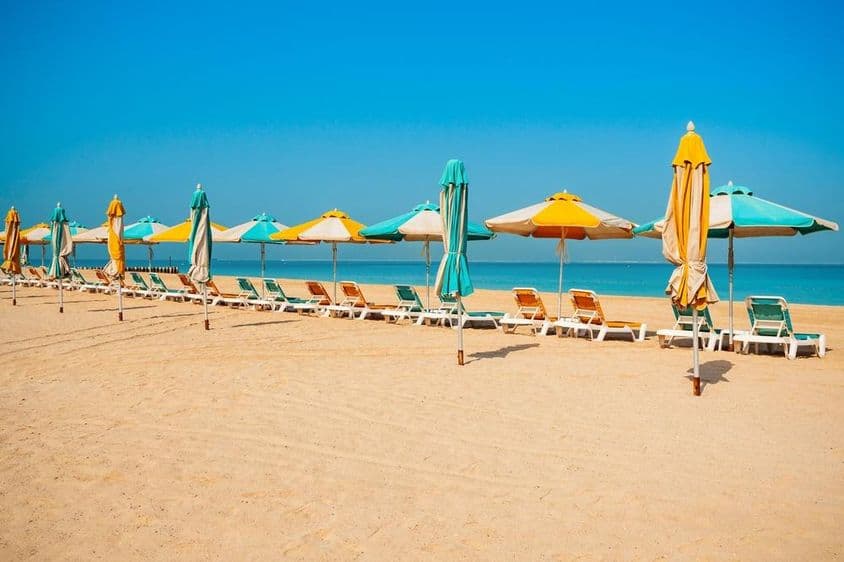 दुबई सार्वजनिक बीच, रेतीला तट, सन लाउंजर्स और नीला समुद्र।