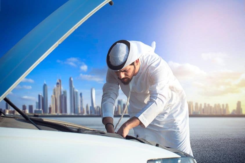 एक अरब व्यक्ति अपनी कार निरीक्षण करते हुए, हुड खुला हुआ।