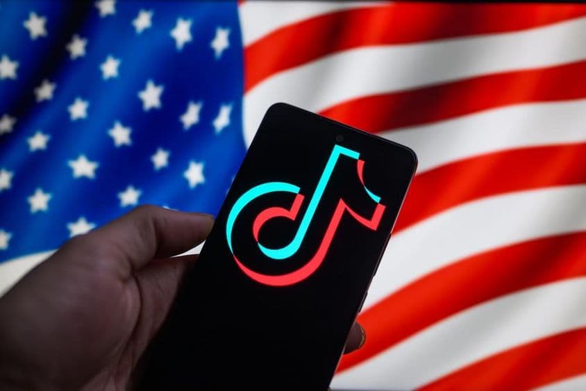 स्मार्टफ़ोन पर प्रदर्शित TikTok का लोगो, जिसके पीछे अमेरिकी झंडा है।