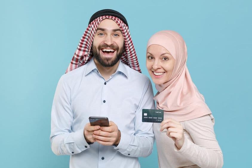 हंसते हुए जोड़े ने क्रेडिट कार्ड और फोन पकड़ा हुआ है।