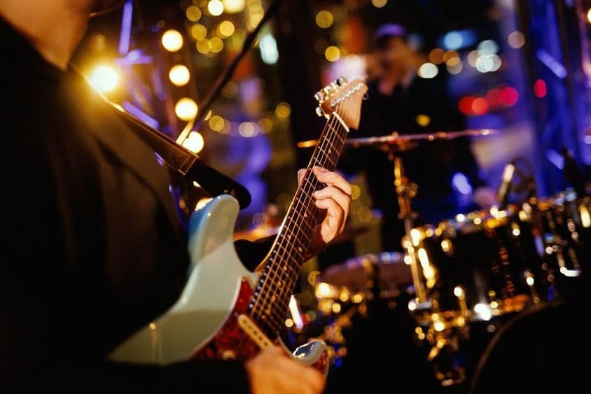 बैंड के प्रदर्शन के दौरान एक गिटारिस्ट गिटार की फेटबोर्ड पर एक कॉर्ड बजाते हुए।