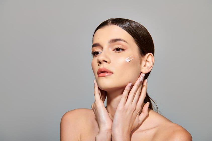 एक युवा महिला अपने चेहरे पर ब्यूटी क्रीम लगाती हुई, आत्म-देखभाल का अनुभव करती है।