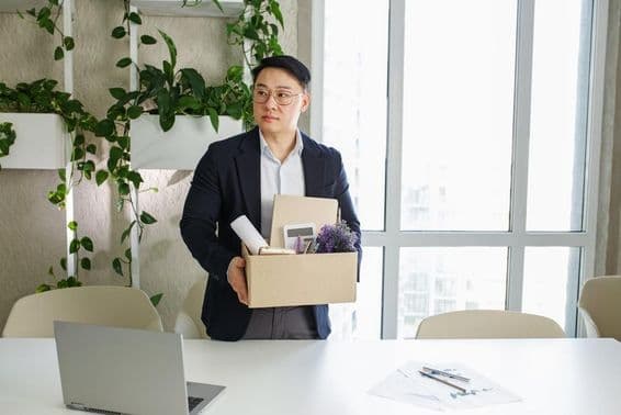 एक व्यक्ति अपने कार्यस्थल से निकाले जाने पर, अपने व्यक्तिगत सामान को एक कार्डबोर्ड बॉक्स में पैक करते हुए।