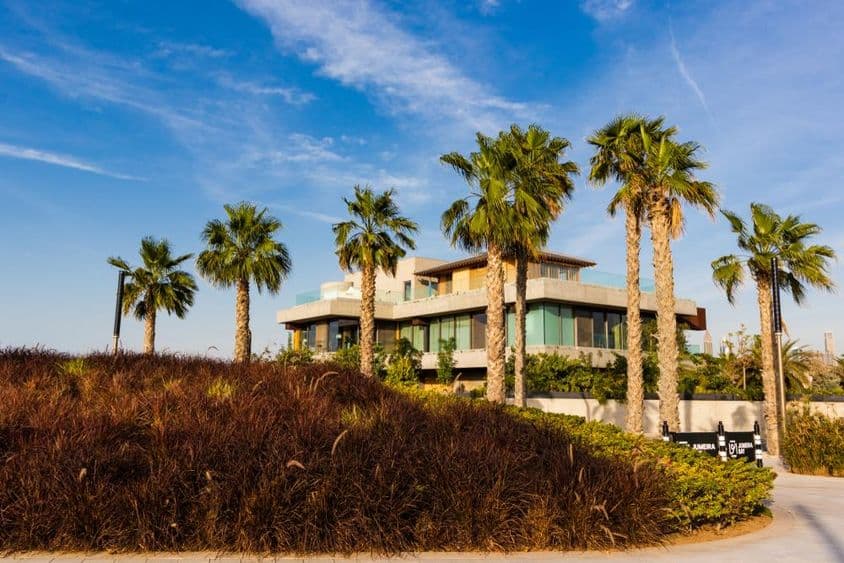 दुबई, खजूर के पेड़ों से घिरा विला एक बादलों भरे सूर्यास्त के परिदृश्य के साथ।