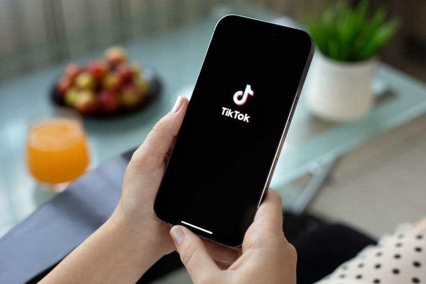 एक महिला के हाथ में एप्पल आईफोन 15 प्रो मैक्स, स्क्रीन पर TikTok वीडियो।