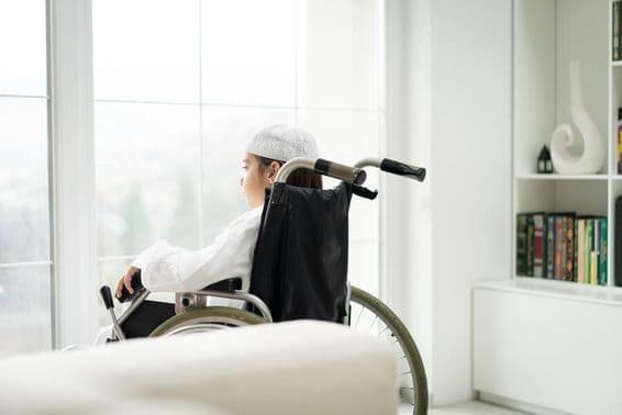 खिड़की के बाहर देखता हुआ व्हीलचेयर में एक युवा लड़का।