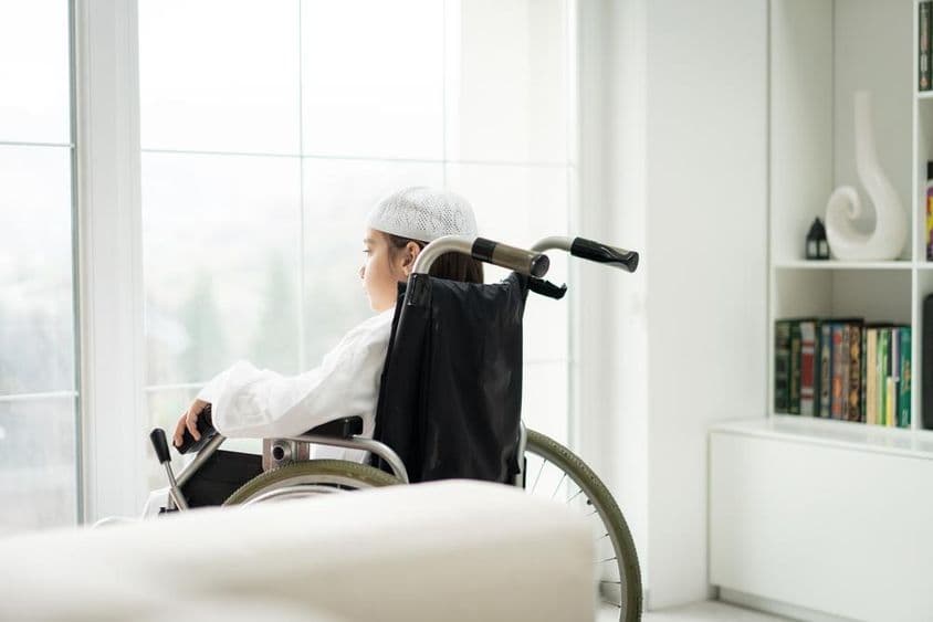 खिड़की के बाहर देखता हुआ व्हीलचेयर में एक युवा लड़का।