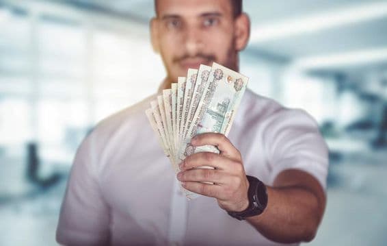 एक व्यक्ति के हाथों में एमिरेट्स दिरहम नकद।
