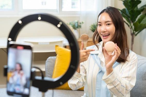 युवा इन्फ्लुएंसर महिला ब्लॉगर स्मार्टफोन का उपयोग करते हुए एक वीडियो स्ट्रीमिंग पॉडकास्ट में बोलते हुए।