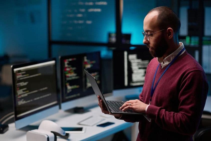 आईटी और साइबर सुरक्षा कार्यालय में एक ओपन लैपटॉप पकड़े हुए कंप्यूटर प्रोग्रामर।