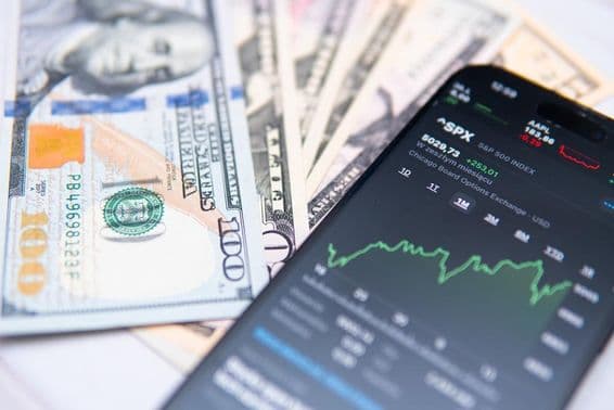 स्मार्टफोन स्क्रीन पर एसपी500 इंडेक्स, अमेरिकी डॉलर पृष्ठभूमि के साथ।
