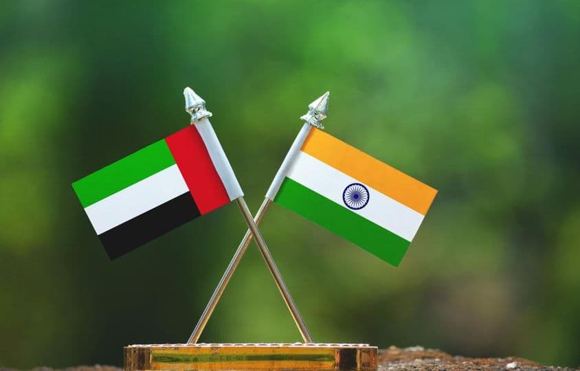 भारत और यूएई के छोटे झंडे एक धुंधली हरी पृष्ठभूमि के खिलाफ।