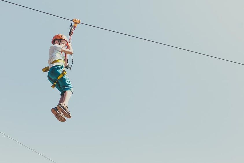 गर्मी की धूप में एडवेंचर पार्क में चढ़ाई करता हुआ लड़का।