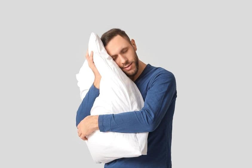 पजामा में एक युवा व्यक्ति कोमल तकिया के साथ।