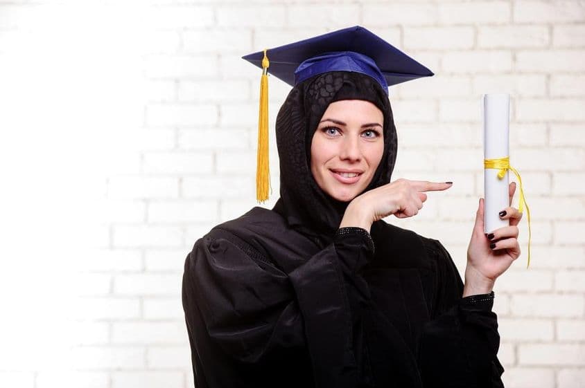 खुश मुस्लिम स्नातक डिप्लोमा के साथ अंदर पोज़ करते हुए।