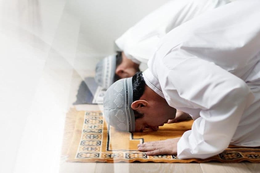 सफेद वस्त्रों में इस्लामी पुरुष प्रार्थना में झुकते हुए।