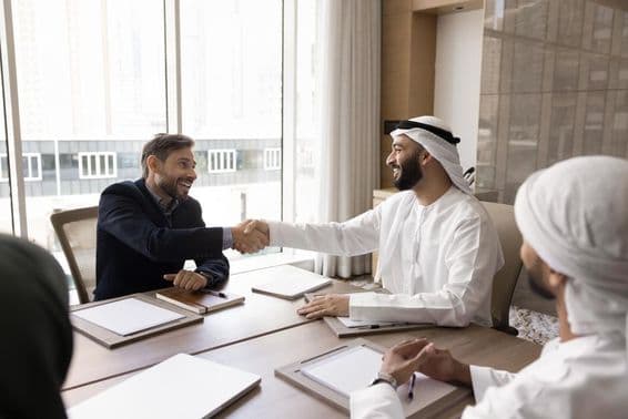 मल्टीनैशनल व्यापारिक साझेदार एक सफल नेगोशिएशन के बाद हाथ मिलाते हुए।