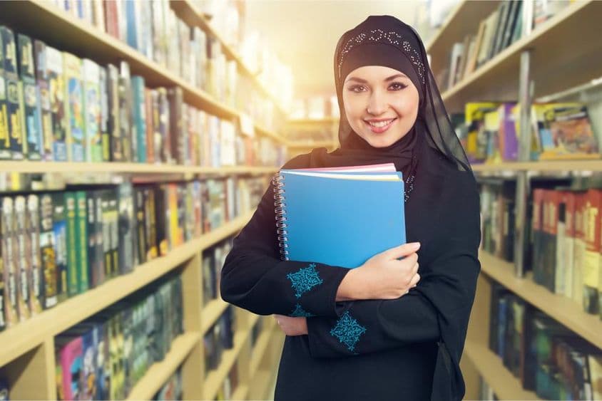 एक पुस्तकें लिए लाइब्रेरी में खड़ा अरब छात्र।