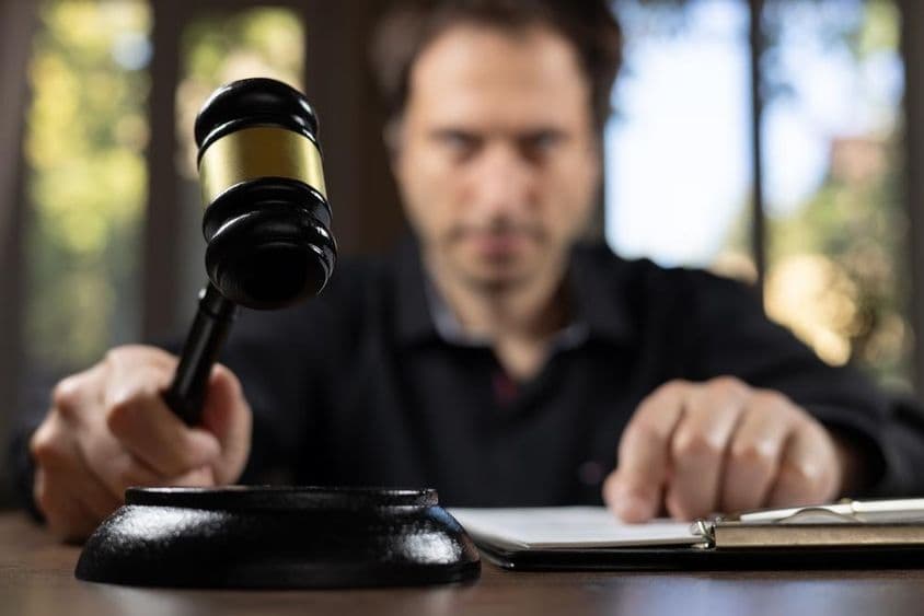 एक न्यायाधीश जो अदालत का हथौड़ा पकड़कर मुकदमे के अंत का संकेत दे रहा है।