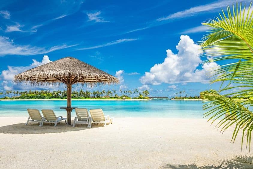 मालदीव की रेतीली समुद्र तट पर छतरी और डेक कुर्सी।