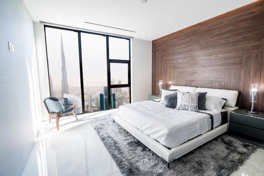 लक्जरी बेडरूम जिसमें सफेद छत और लकड़ी का ट्रिम है, जिससे दुबई शहर का नज़ारा दिखता है।