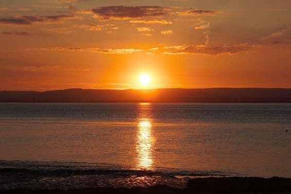 ग्रीष्मकालीन विषुव के दौरान पानी और बादलों पर प्रतिबिंबित सूर्यास्त।