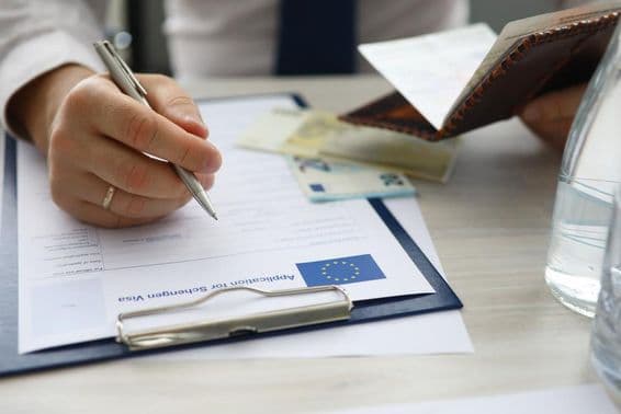 एक व्यक्ति पासपोर्ट पकड़े हुए और शेंगेन वीज़ा आवेदन पर व्यक्तिगत जानकारी दर्ज कर रहा है।