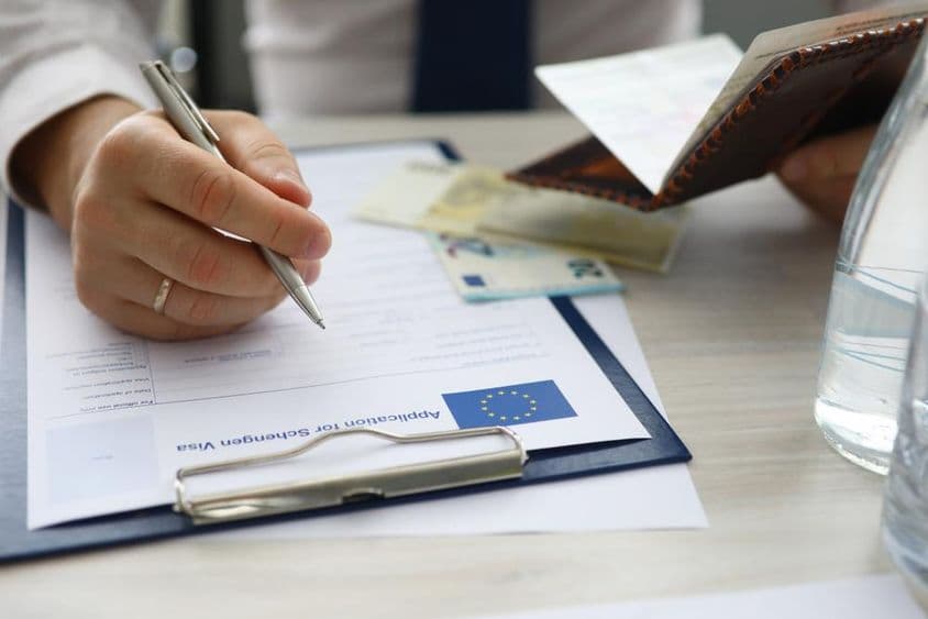 एक व्यक्ति पासपोर्ट पकड़े हुए और शेंगेन वीज़ा आवेदन पर व्यक्तिगत जानकारी दर्ज कर रहा है।