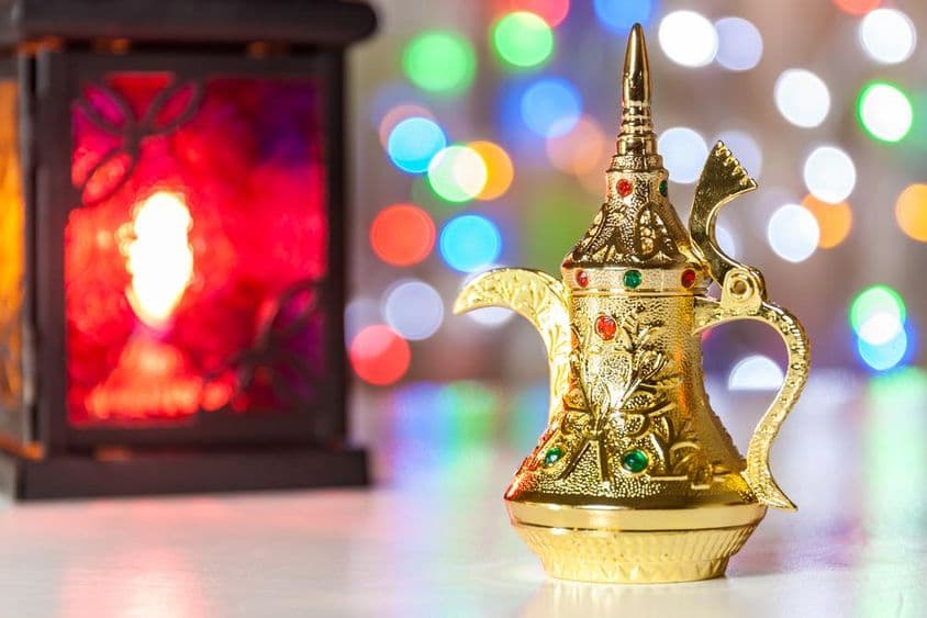 अरबियन कॉफी पॉट और लालटेन जिसके पीछे रंग-बिरंगी, धुंधली रोशनी।