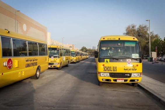 अबू धाबी में एक कतार में खड़ी और खड़ी पीली स्कूल बसें।